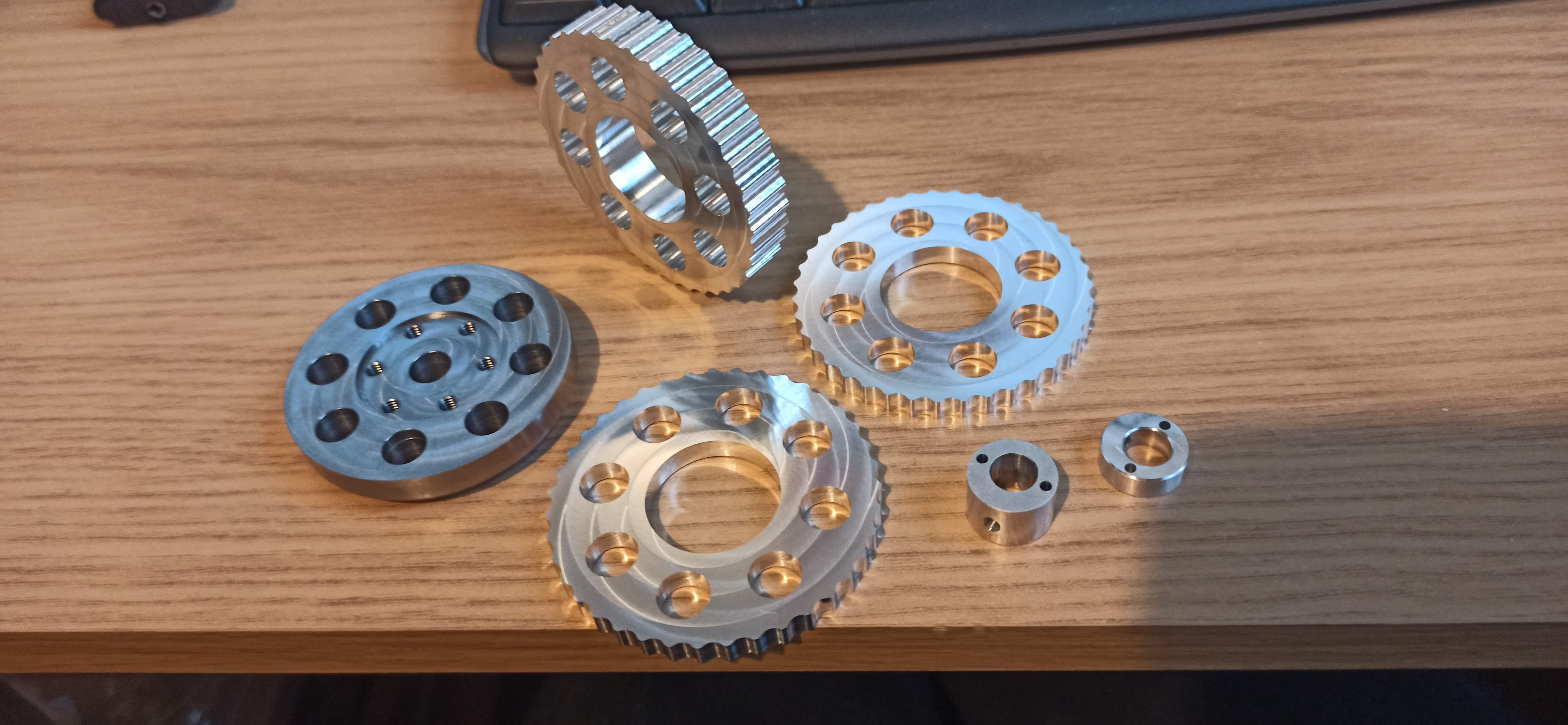 Freshly machined aluminium cycloidal discs, ring gear and eccentric hubs laid out on a desk beside a keyboard